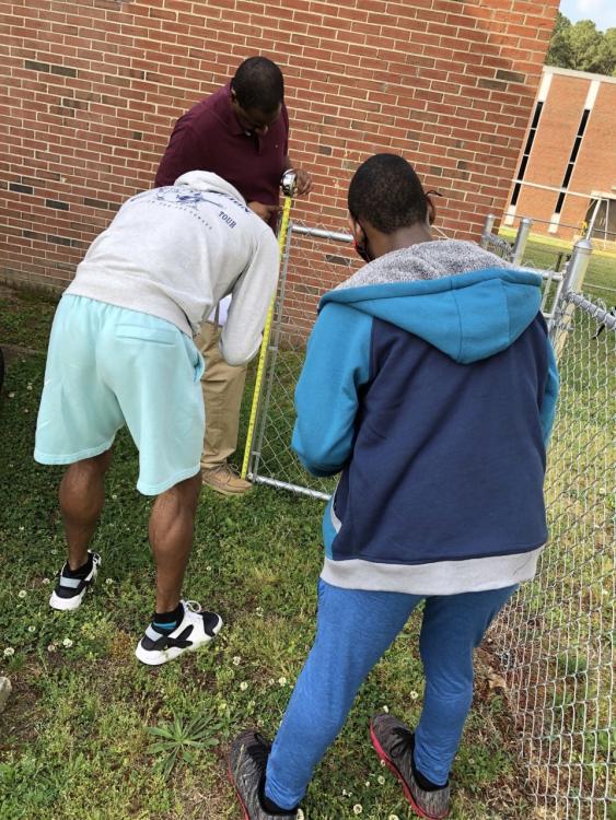 Students measuring dimensions of a fence gate