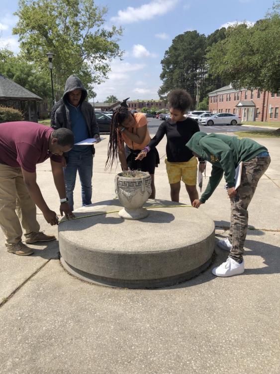 Students measuring dimensions of a cement planter