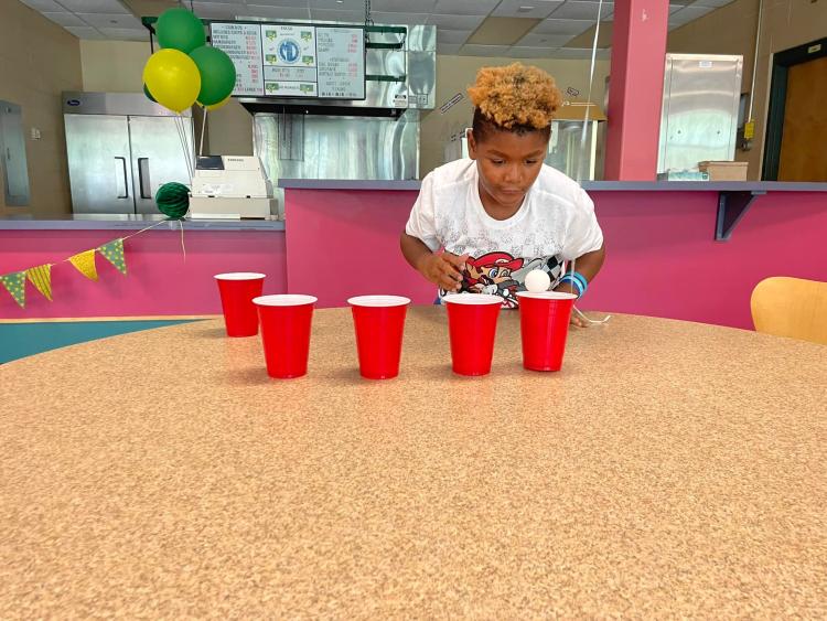 Student playing a game with a ping pong ball and cups