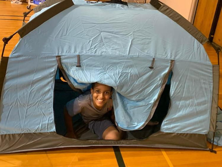 Student peeking out of tent in the gym