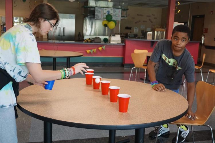 Student playing a game with a ping pong ball and cups