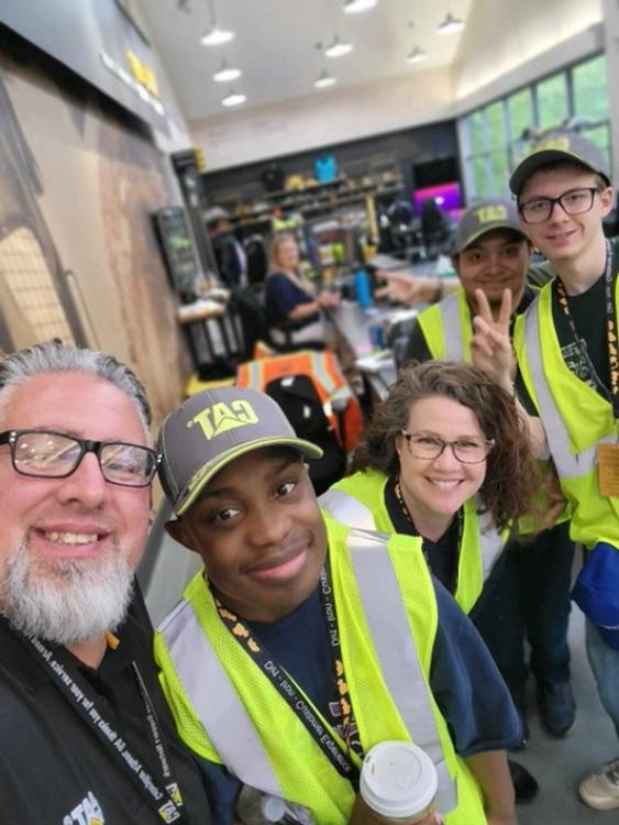 Students and staff pose with Caterpillar employee