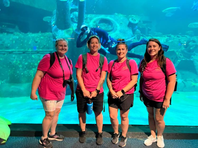 Natasha, Heather, Krystal, Michaela stand in front of large aquarium with diver in it.